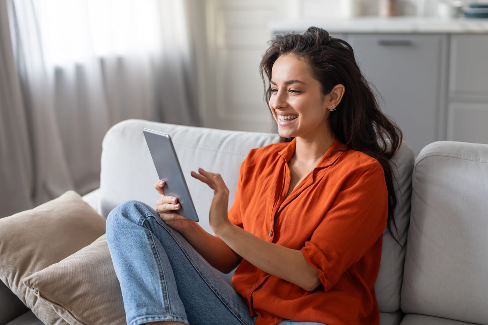 57267202_smiling-woman-in-orange-shirt-using-tablet-on-comfortable-sofa-at-home.jpg